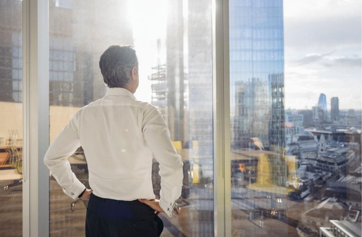 Business owner standing by office window looking out over city, reflecting during a moment of financial stress